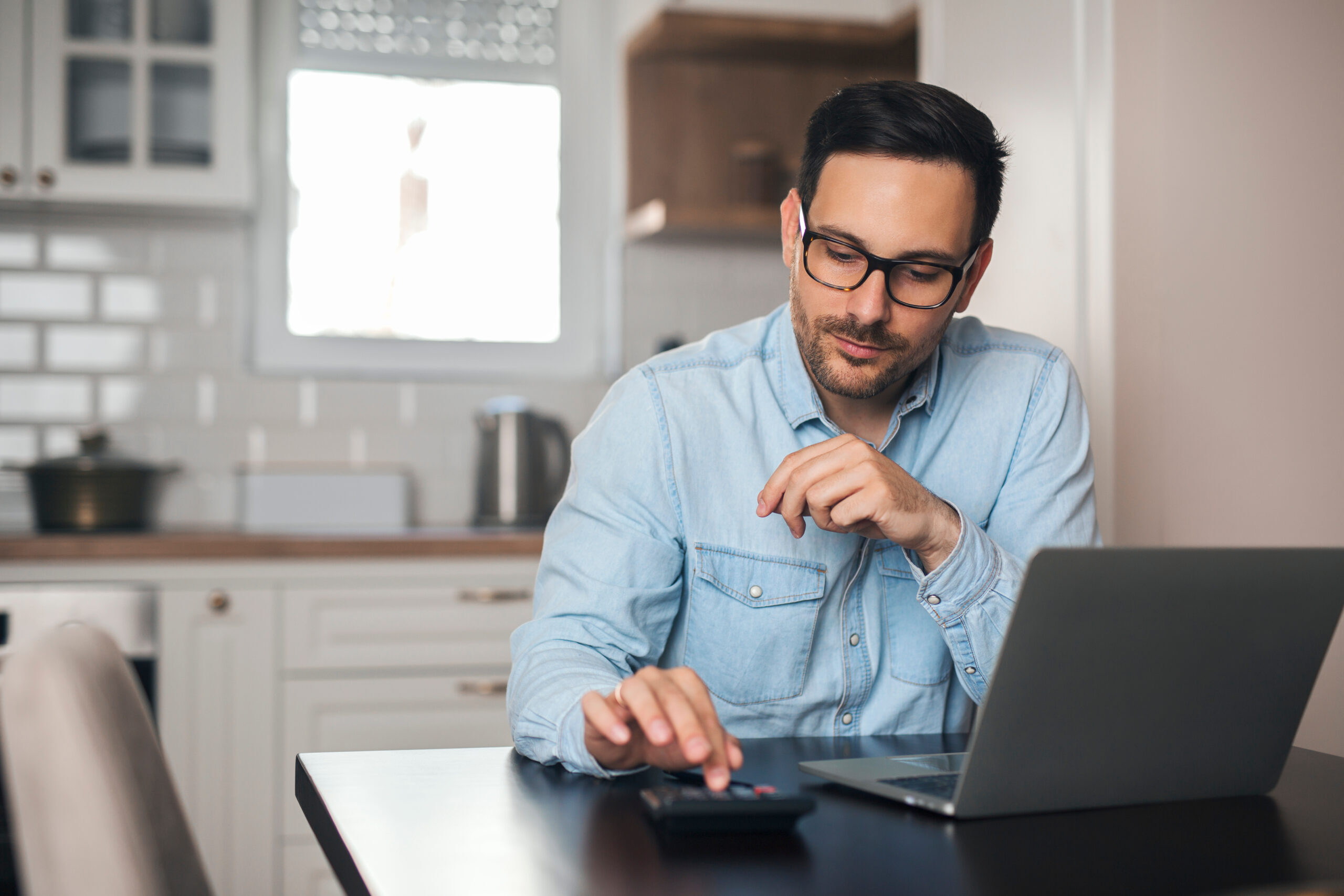 Senior Couple Sitting Around Table At Home Reviewing Finances Using Digital Tablet